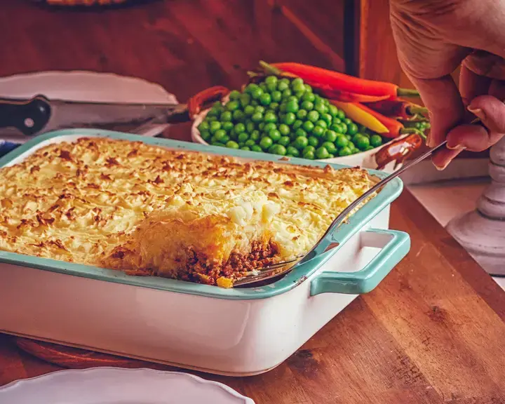 Someone spooning cottage pie from a casserole dish.