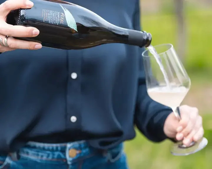 A person pouring a Feral drink into a wine glass.