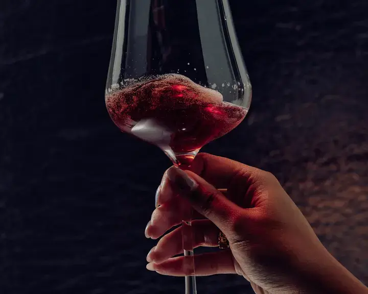 A woman's hand holding a wine glass of red Non, non-alcoholic beverage.
