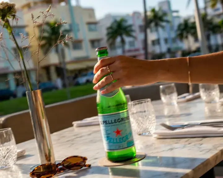A hand holding a S.Pellegrino bottle on a Miami restaurant terrace.
