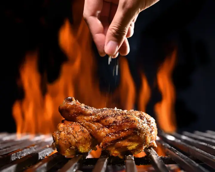Chicken on the barbecue being seasoned.