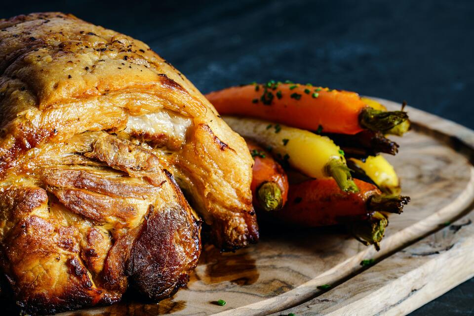 Roasted meat with golden and orange carrots served on a rustic plate.