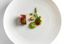 Elegant gourmet dish with seared meat, green purée, asparagus, tiny flowers and artful sauce dots on a minimalist white plate